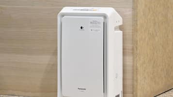 A white Panasonic air conditioner unit with a water tank on the side, placed against a tiled wall.