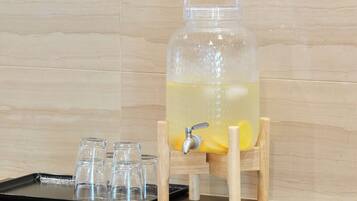 A clear glass pitcher on a wooden stand with a tap, filled with a yellow liquid, accompanied by a tray of empty glasses.