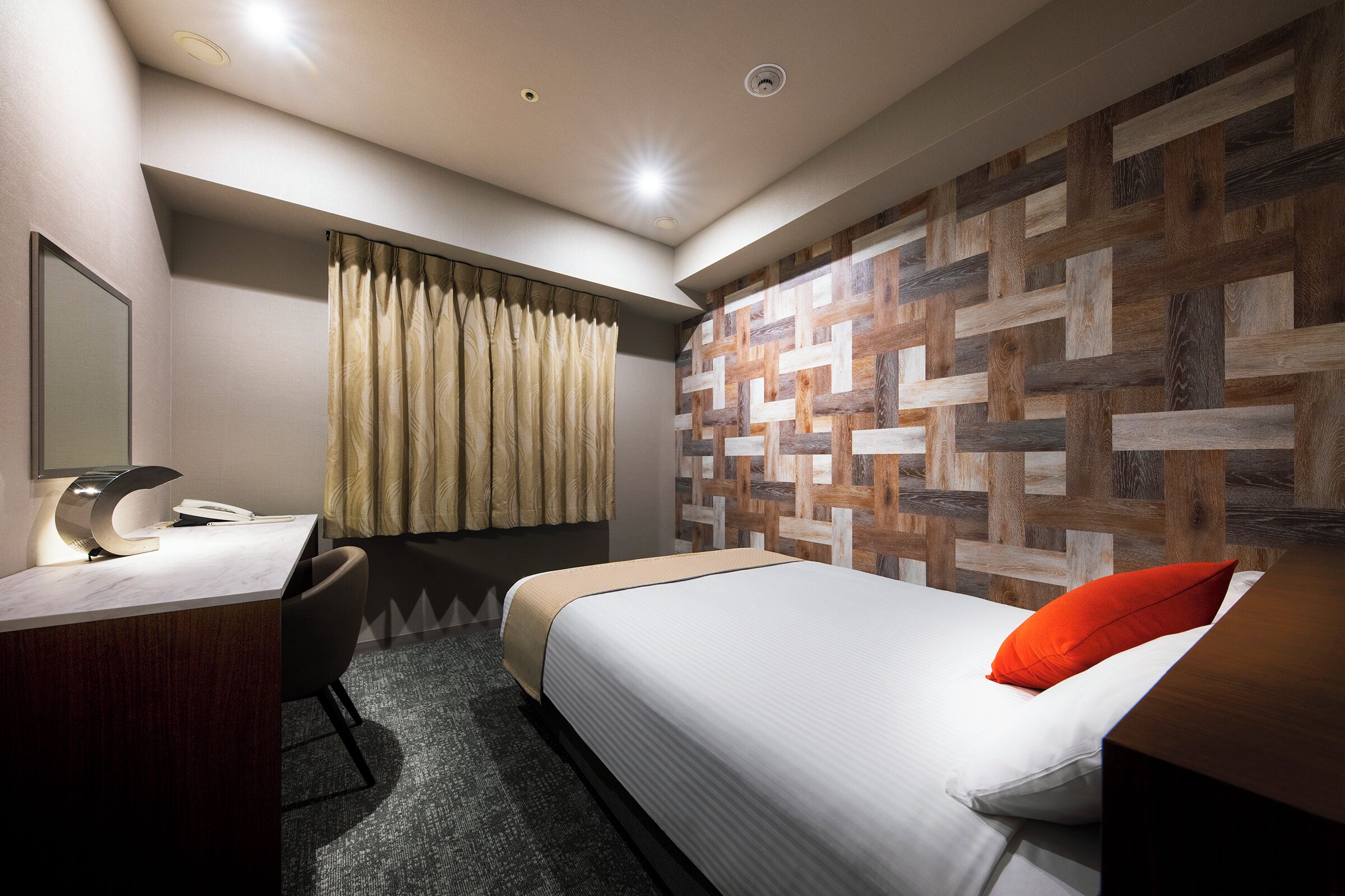 A hotel room with a desk, chair, bed, and a wall with a geometric pattern.
