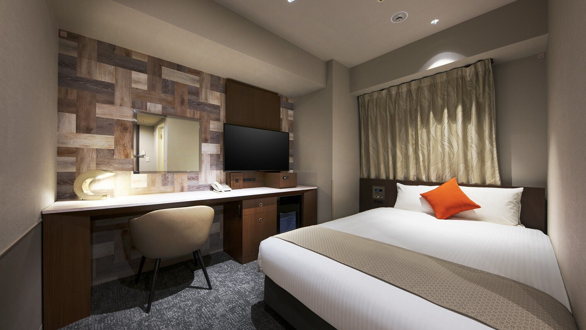 A hotel room with a bed, a desk with a chair, a television, and a mirror.