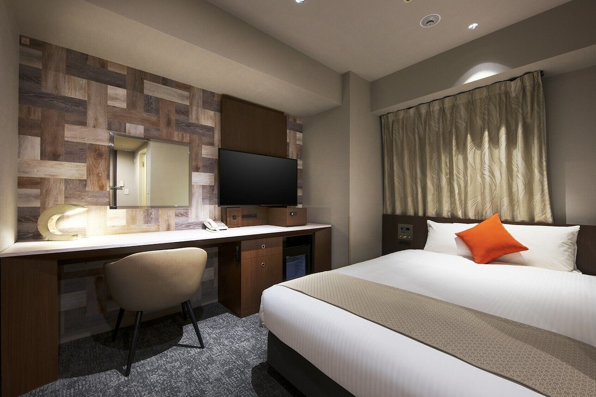 Een hotelkamer met een bed, een bureau met stoel, een televisie en een spiegel.