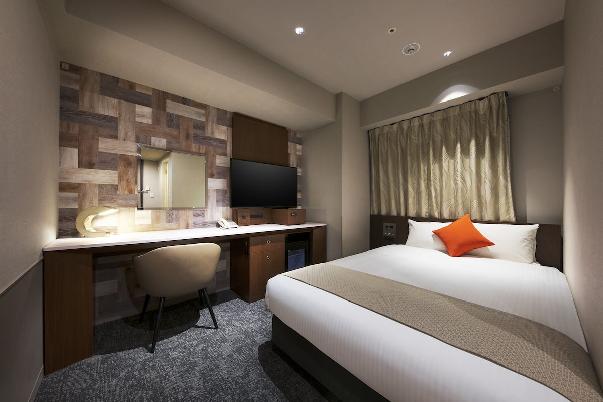Een hotelkamer met een bed, een bureau, een stoel, een televisie en een raam met gordijnen.