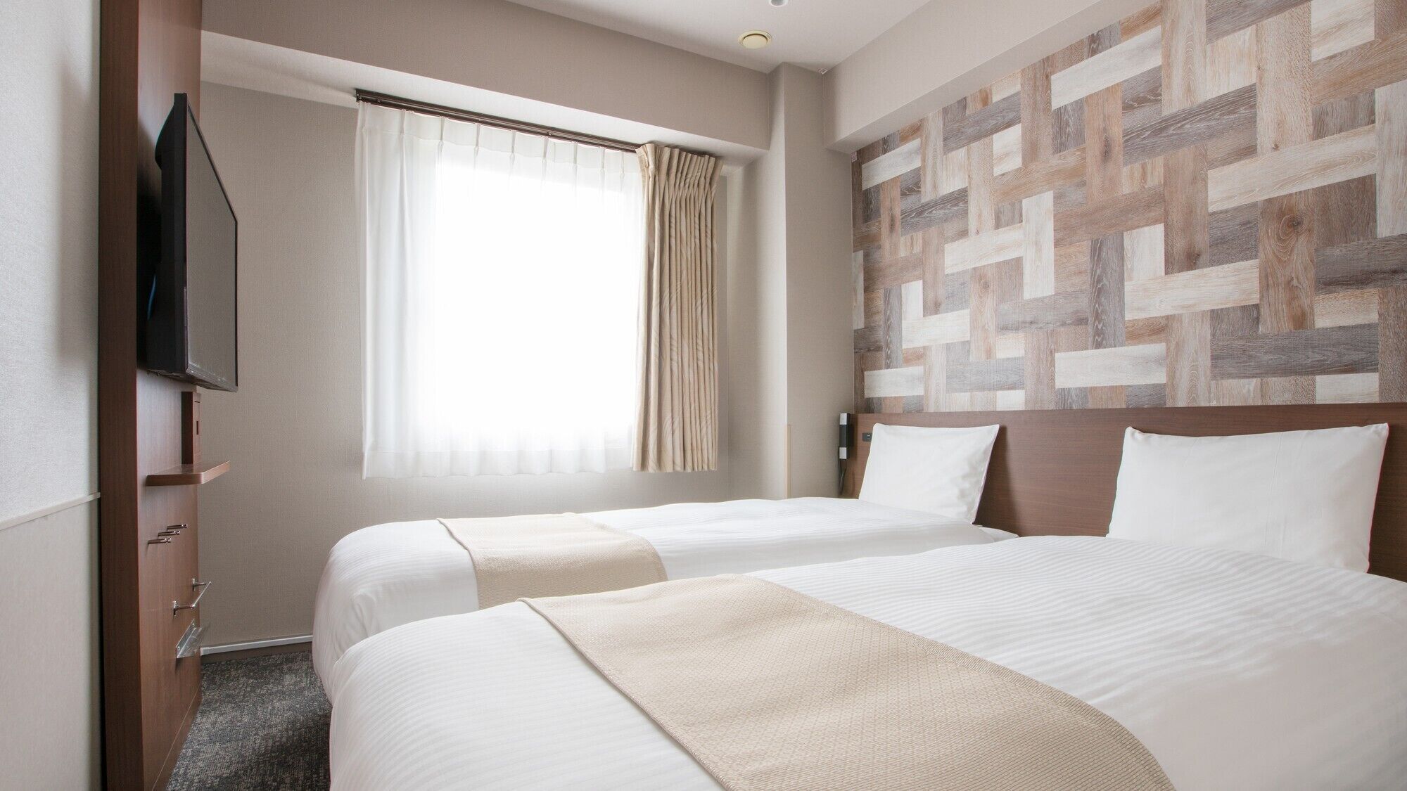 A hotel room with two beds, a TV, a window with curtains, and a wooden wall panel.