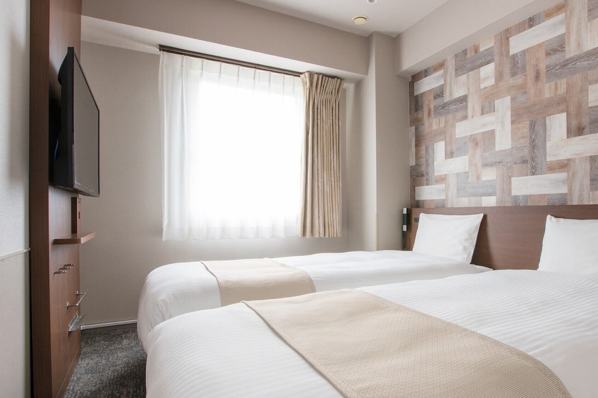 Een hotelkamer met twee bedden, een televisie, een raam met gordijnen en een houten wandpaneel.
