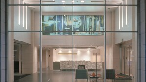 Eine moderne Hotelhalle mit Glastrennwand, einer Rezeption und einem großen abstrakten Gemälde.