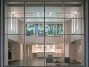 Eine moderne Hotelhalle mit Glastrennwand, einer Rezeption und einem großen abstrakten Gemälde.