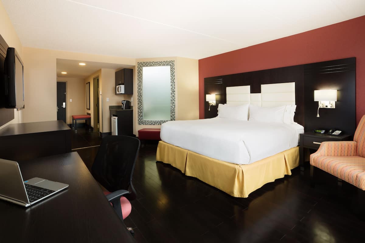 Hotelkamer met een groot bed, een bureau met een laptop, een stoel, een televisie en een kleine kitchenette.