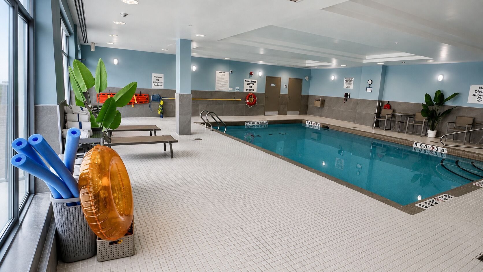 An indoor swimming pool with clear lane markings, safety signs, and a lifeguard chair.