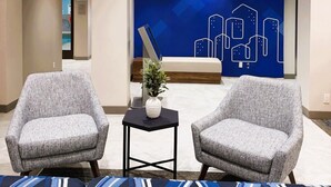 Een hal met twee grijze fauteuils, een bijzettafeltje met een vaas en een blauwe muur met een stadsgezicht.