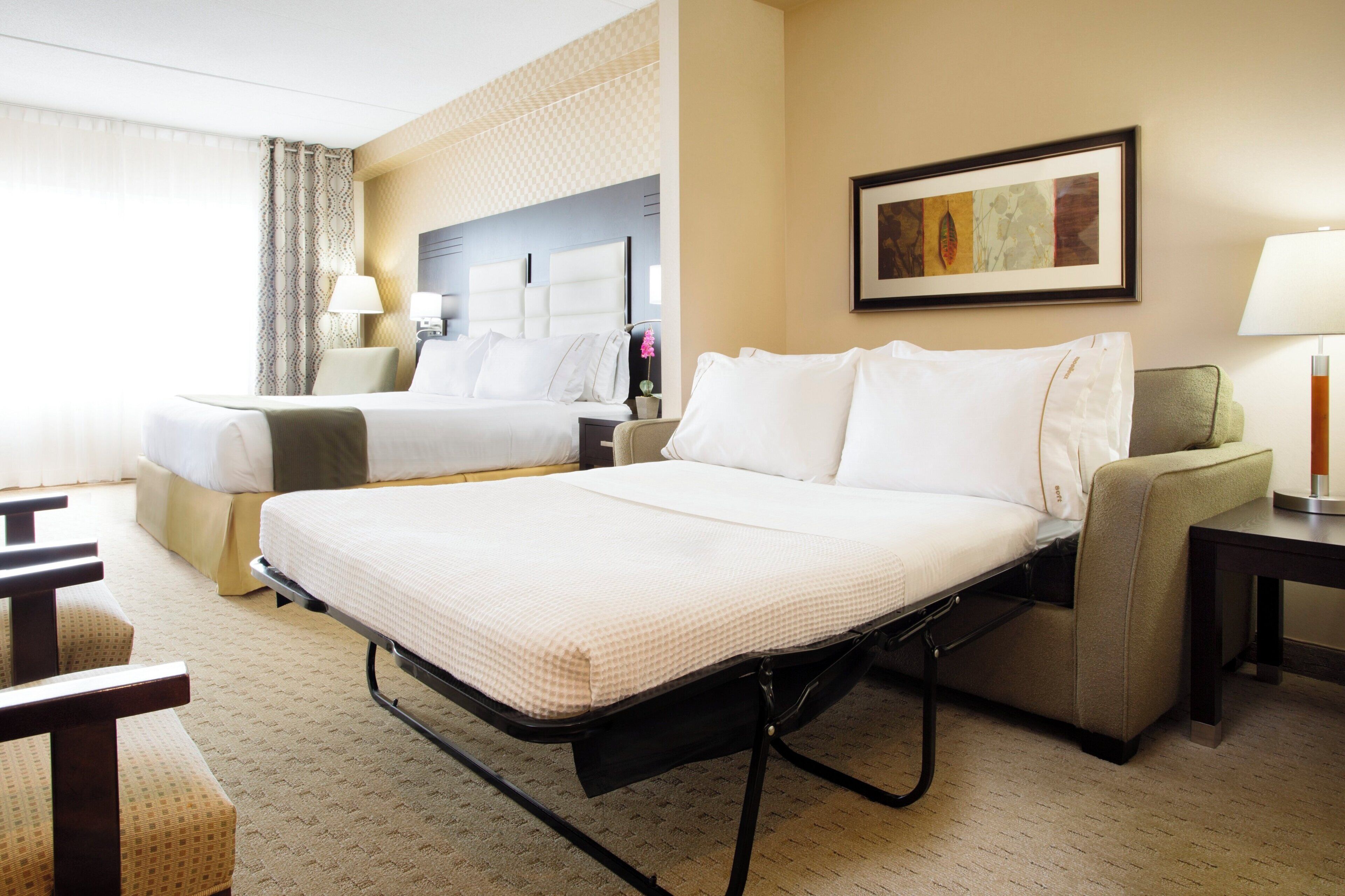 A hotel room with two beds, a sofa, a desk, a lamp, and a painting on the wall.