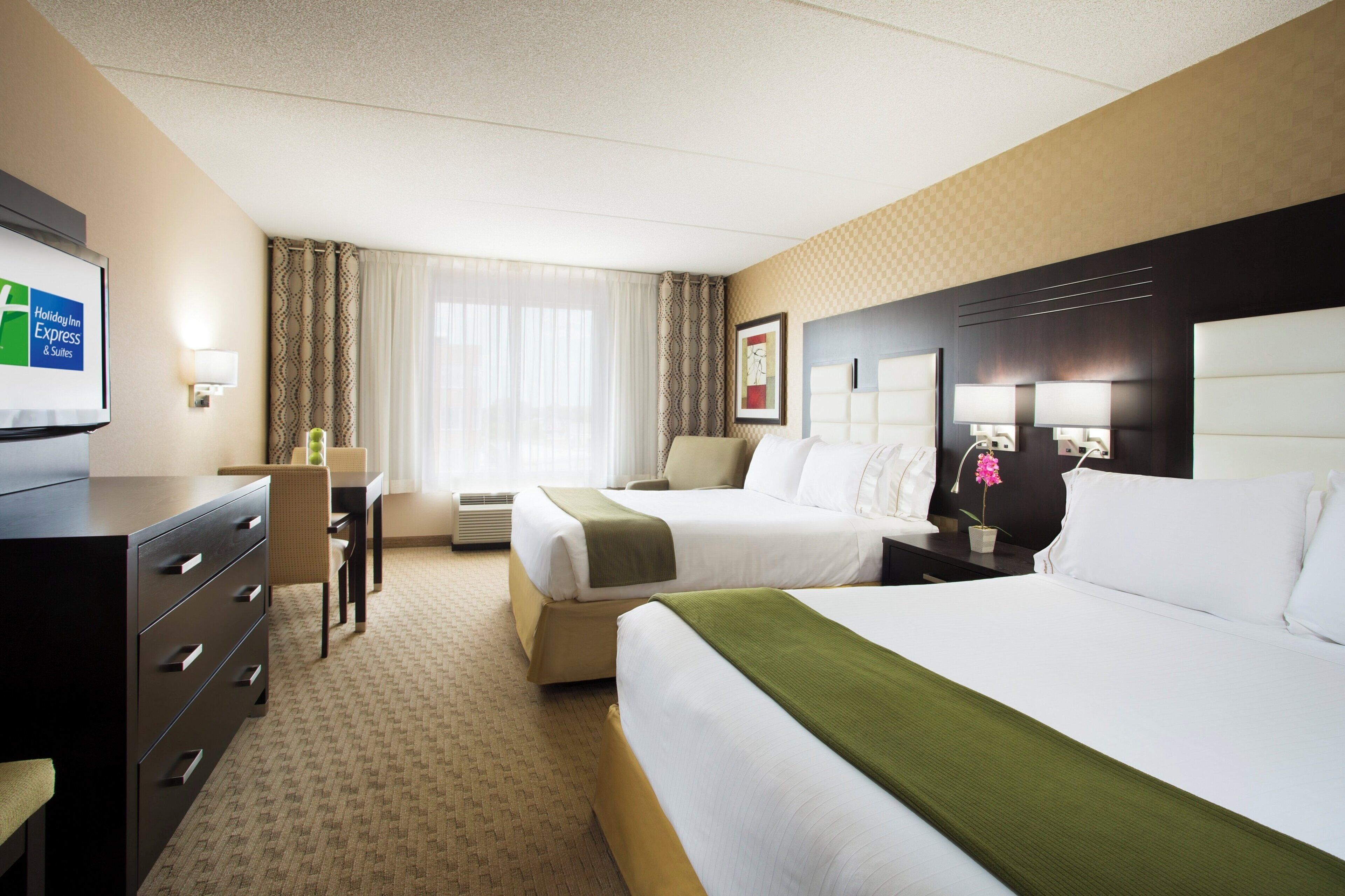 A hotel room with two beds, a desk, a chair, a television, and a window with curtains.