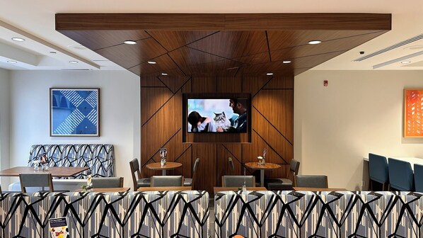 Een moderne hotellobby met een groot televisiescherm, houten lambrisering en een gestructureerd zitgedeelte.
