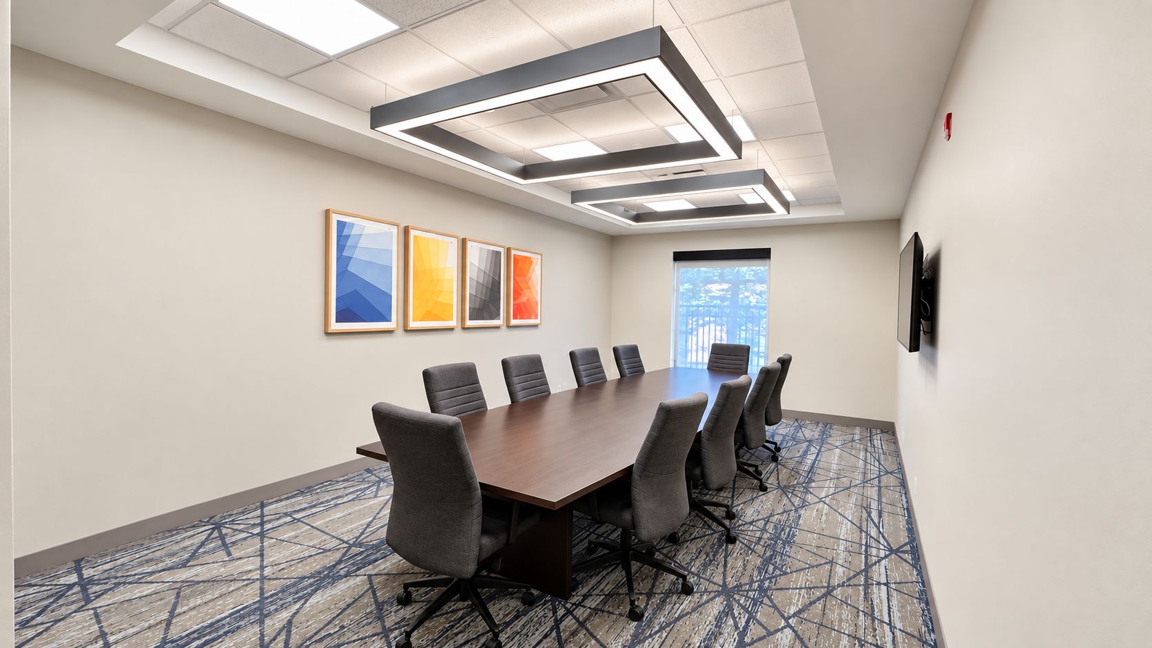 A conference room with a long table, six chairs, and framed artwork on the wall.