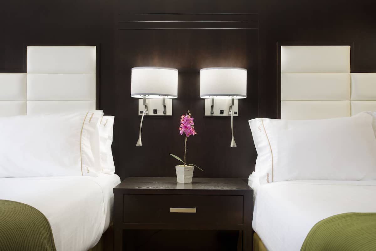 Een hotelkamer met twee bedden, een nachtkastje met lade en twee wandlampen.