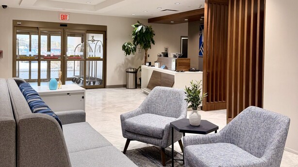 Een moderne lobby met een bank, fauteuils, een receptiebalie en een groot raam.