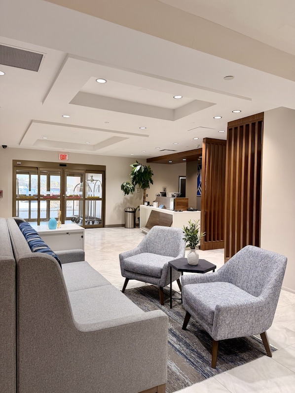 A modern lobby with a sofa, armchairs, a reception desk, and a large window.