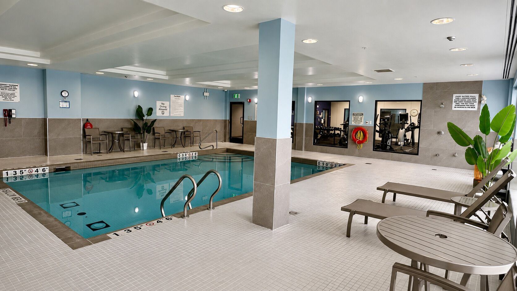 En indendørs swimmingpool med tydelige baneinddelinger, en redningsbåd og et opholdsområde med borde og stole.