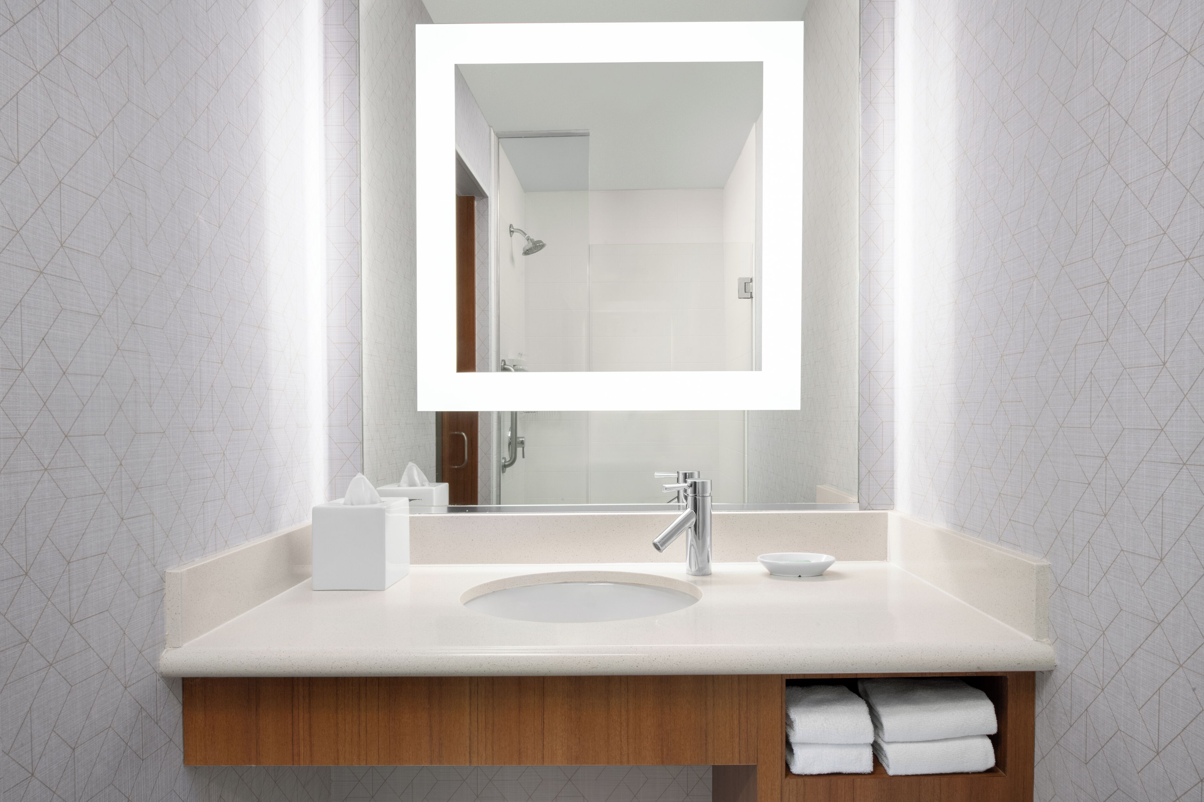 Een moderne badkamer met een grote spiegel, een wastafel en een douche die in de spiegeling te zien is.