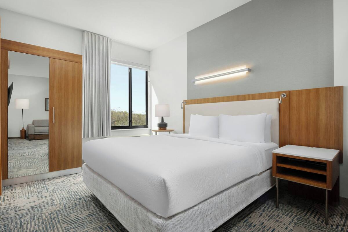 A hotel room with a large bed, a bedside table, a mirror, and a view of the outdoors.