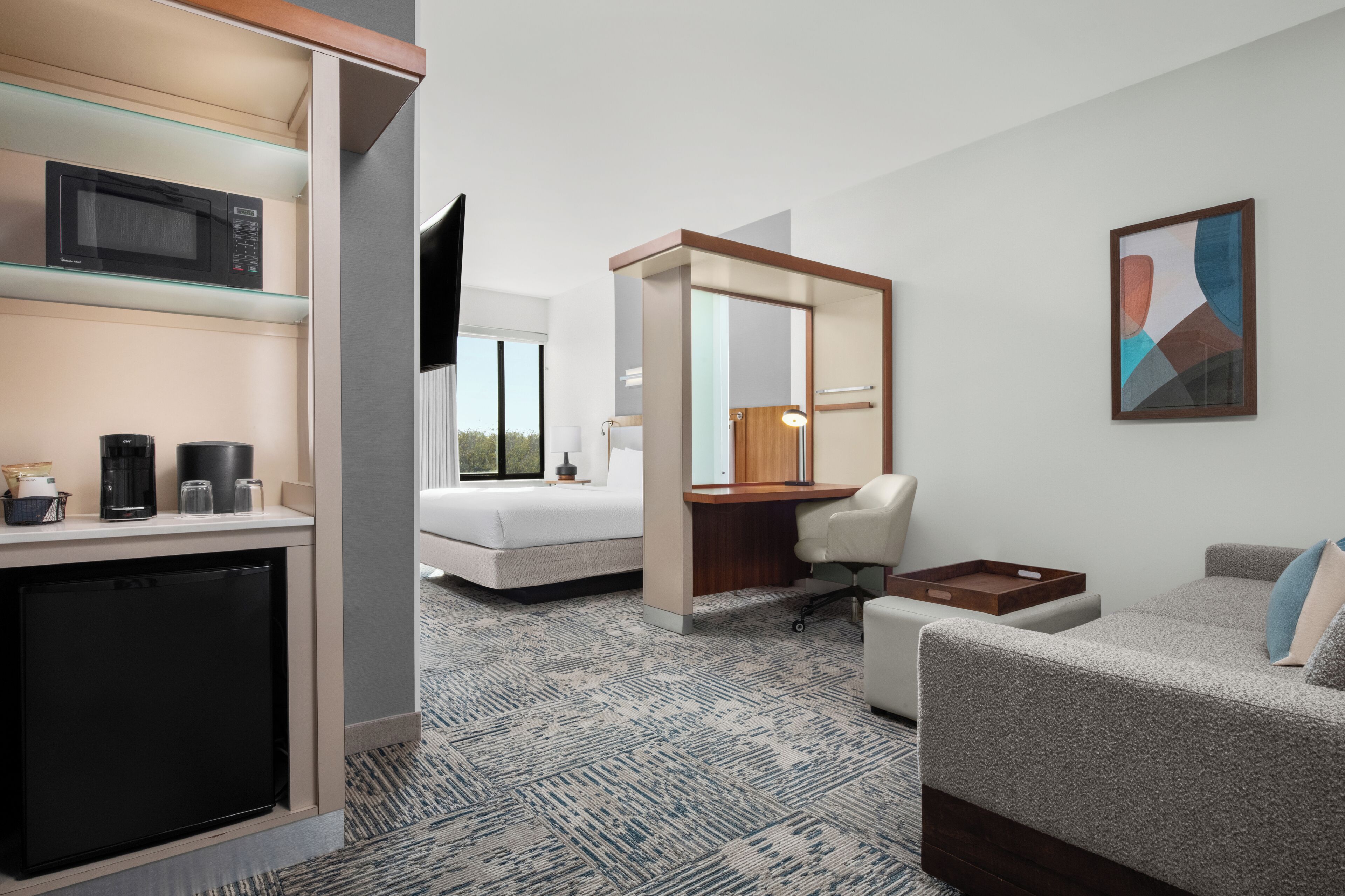 Habitación de hotel con kitchenette, cama, escritorio, silla y un espejo grande.