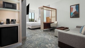 Ein Hotelzimmer mit Küchenzeile, einem Bett, einem Schreibtisch, einem Sessel und einer Couch.