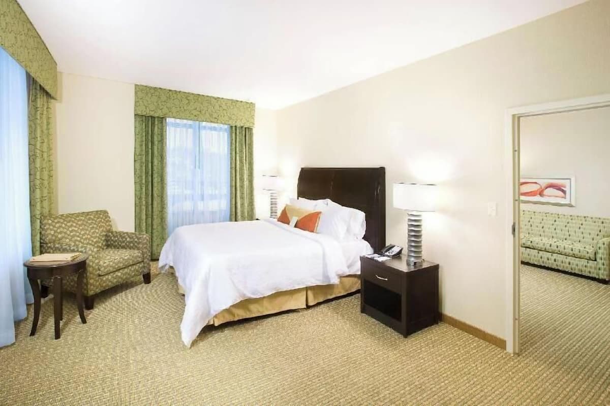 A hotel room with a bed, a chair, a nightstand, and a door.