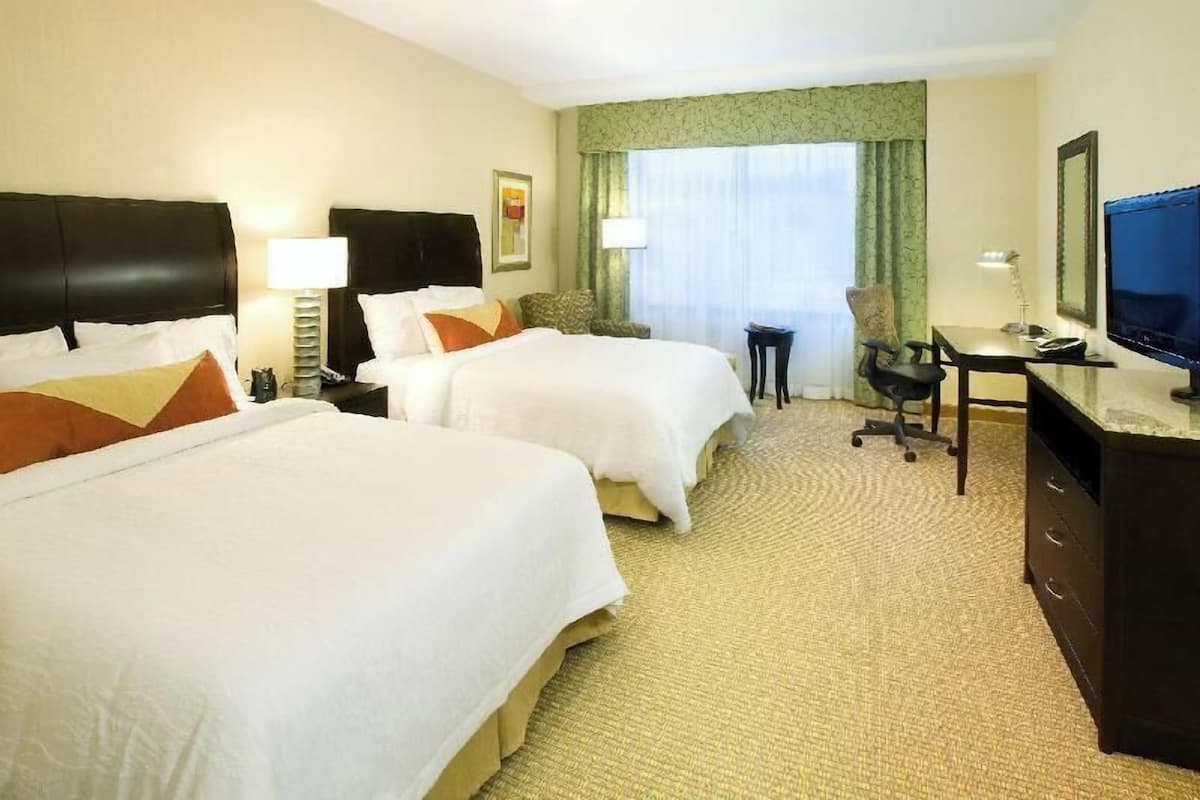 A hotel room with two beds, a desk, a chair, a television, and a window with curtains.