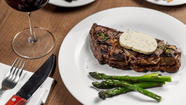 A steak with a slice of cheese on a plate, asparagus, and a glass of red wine. - Hilton Garden Inn Arlington-Shirlington (Arlington)