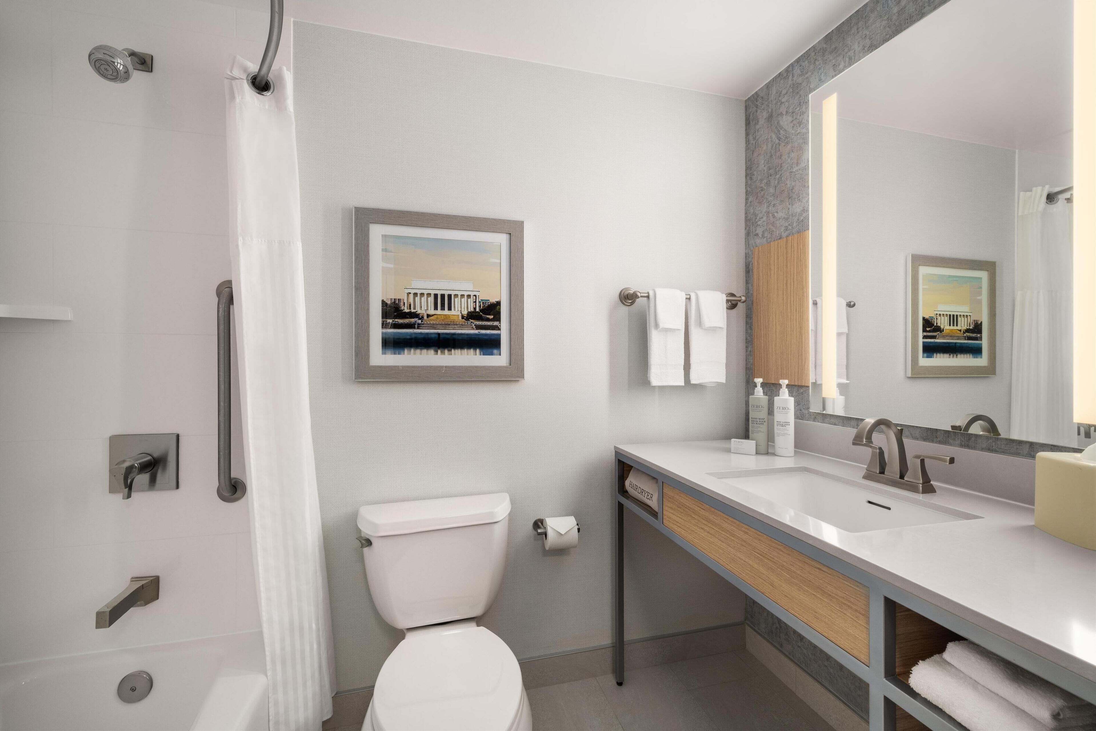 Ein modernes Badezimmer mit Toilette, Waschbecken und Dusche. An den Wänden hängen Bilder in Rahmen, es gibt einen Handtuchhalter und einen Spiegel.