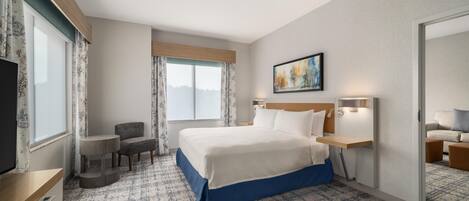 A hotel room with a large bed, a desk, a chair, and a window with curtains.