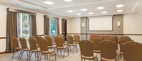 A conference room with rows of chairs, a projector screen, and a large window with curtains.