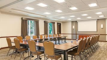 A conference room with a long table, chairs, a projector screen, and windows with curtains.