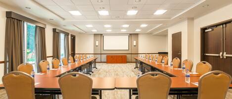 A conference room with a long table, chairs, a projector screen, and a presentation podium.