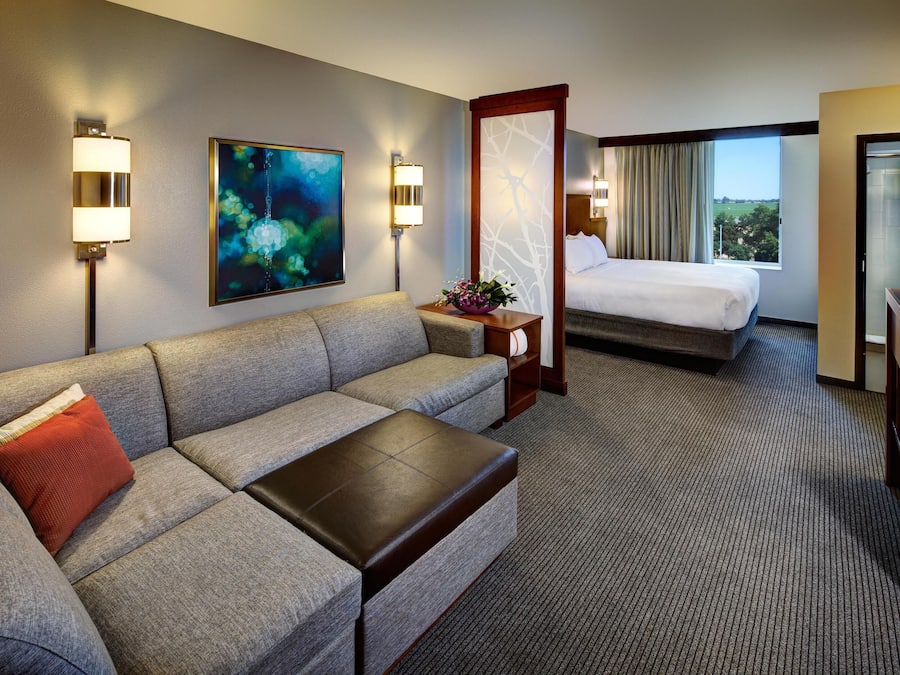 A hotel room with a sofa, a bed, a TV, and a painting on the wall.