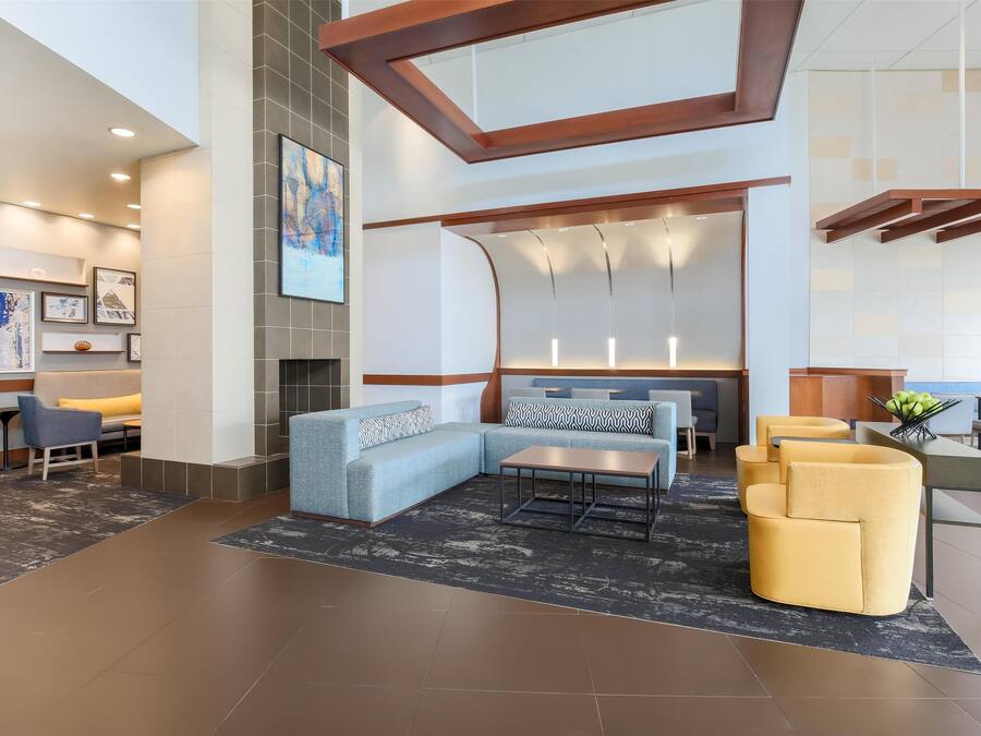 A modern lobby with a sectional sofa, a coffee table, and a dining area with yellow chairs.
