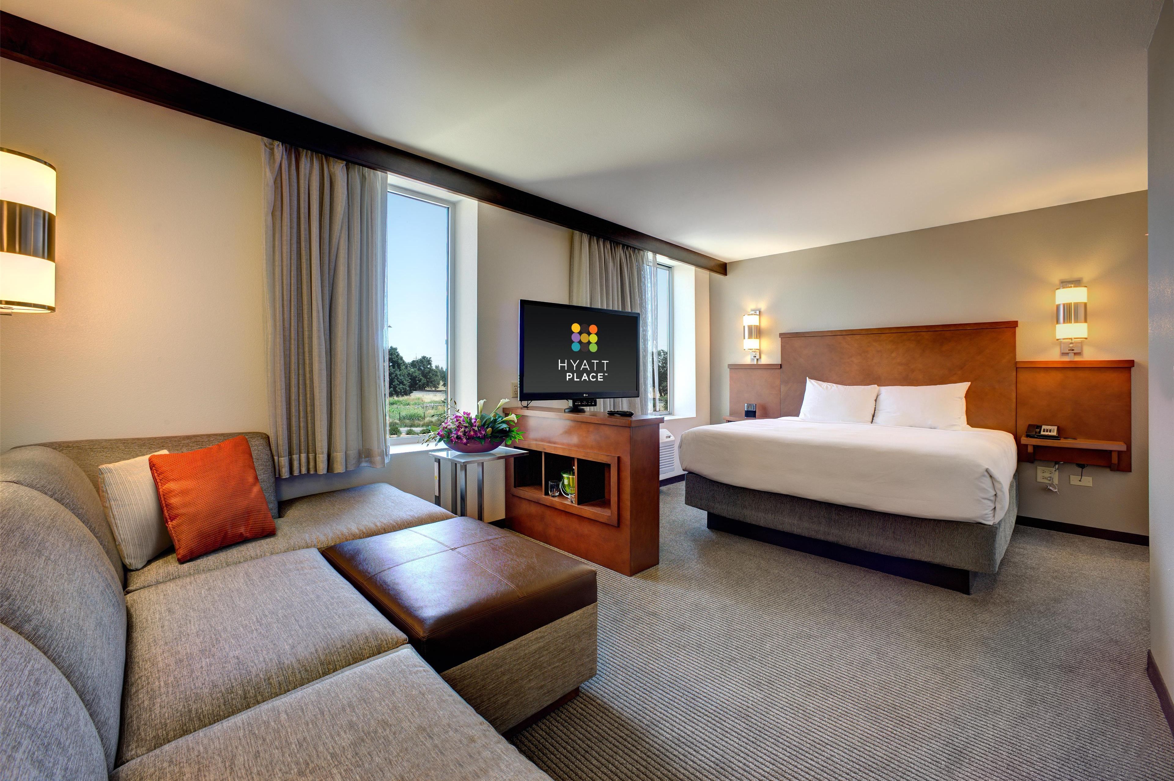 A modern hotel room with a sofa, a bed, a TV, and a view of the outdoors.