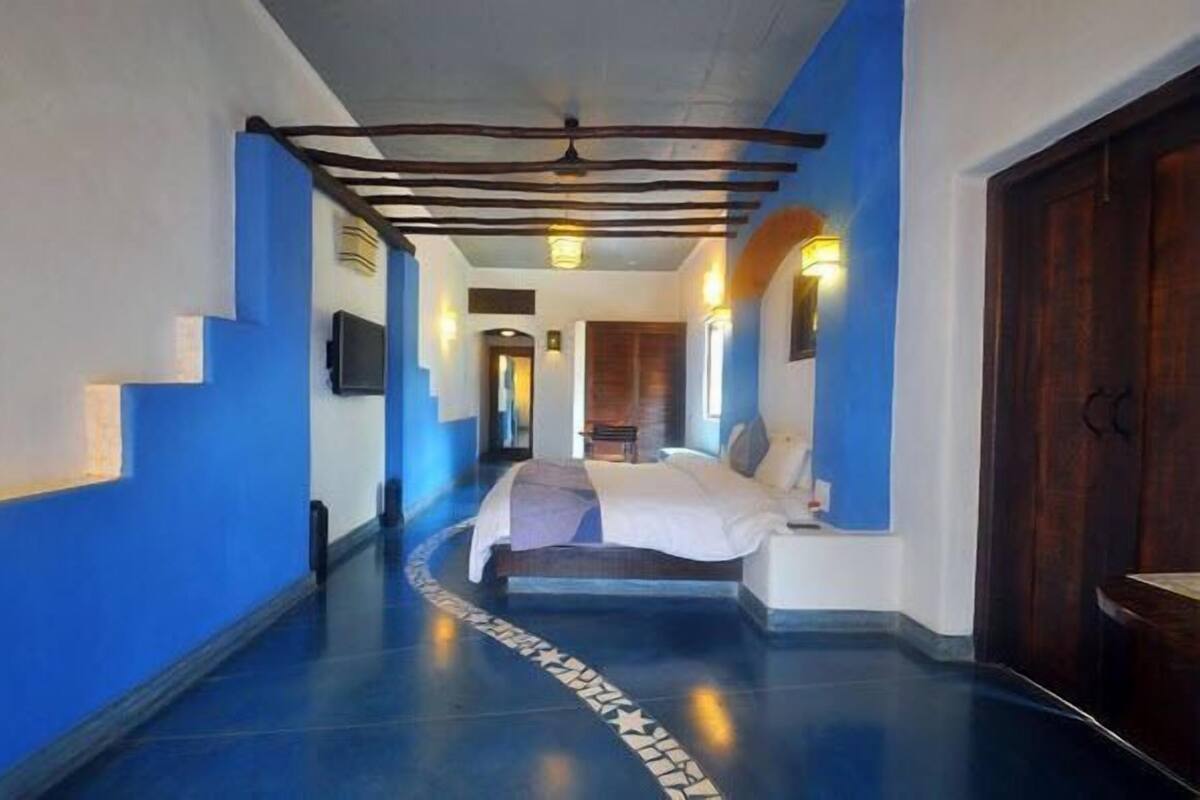 Un couloir d’hôtel avec un lit, des murs bleus et une porte en bois.