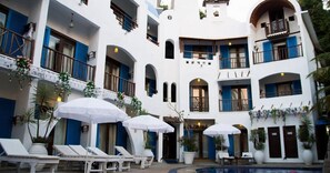 A multi-story building with balconies, a swimming pool, and outdoor seating areas with umbrellas. - Mykonos Blu (Baga)