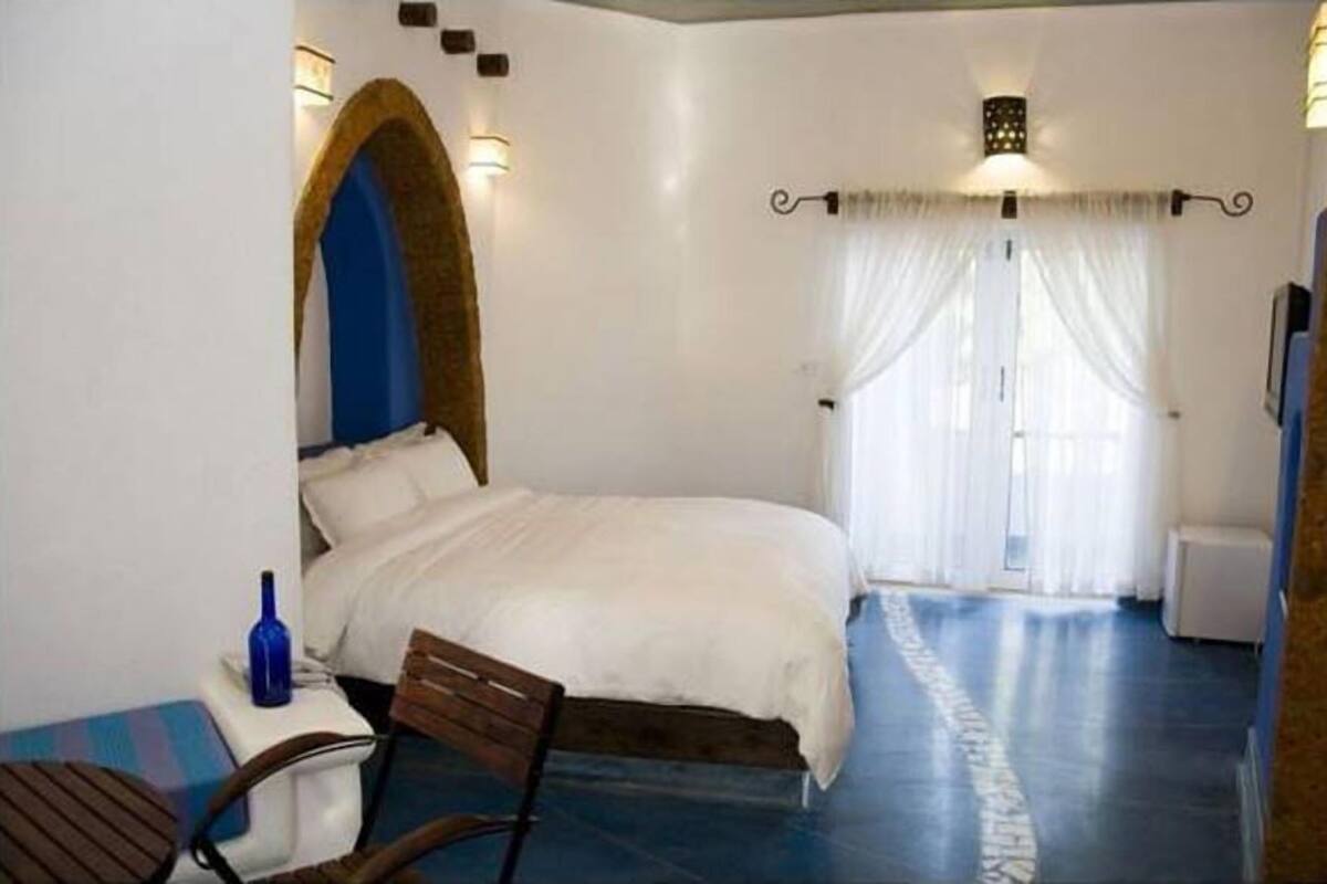 Une chambre à coucher avec un lit, une chaise, une petite table et une bouteille bleue.