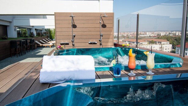 A rooftop hot tub with three drinks, a towel, and a wooden deck with lounge chairs. - Ramada by Wyndham Oradea (Oradea)