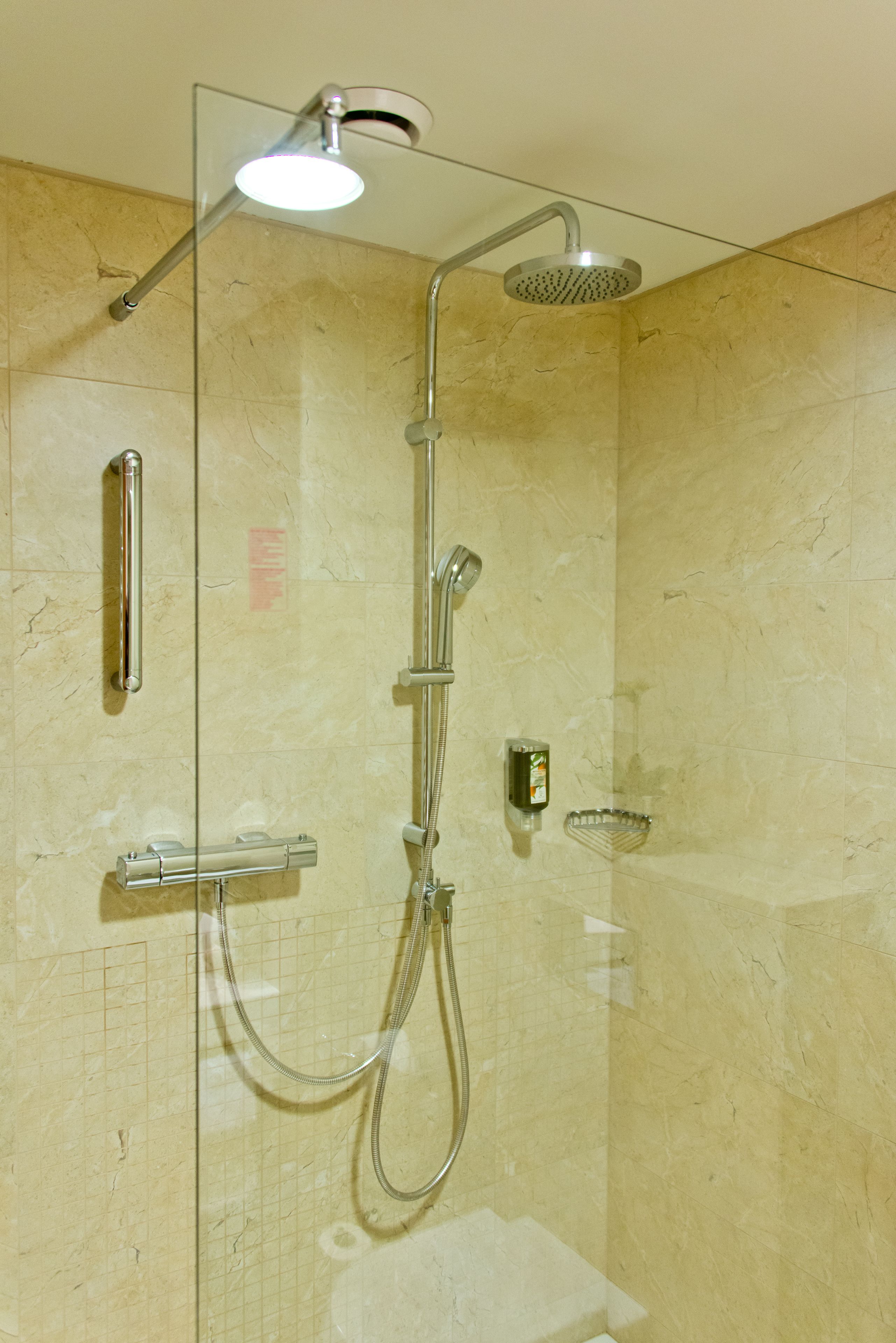 Une douche fermée par des parois en verre, équipée d’un pommeau de douche à main, d’un pommeau de douche fixe et d’un pommeau de douche à main avec une fonction pluie.
