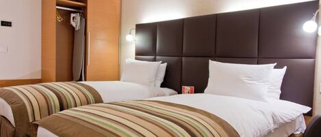 A hotel room with two beds, a wardrobe, and a nightstand with a lamp.