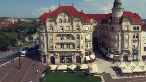 A historic building with a red roof and green spire, featuring a central courtyard with outdoor seating and umbrellas. - Ramada by Wyndham Oradea (Oradea)