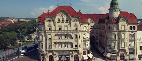 A historic building with a red roof and green spire, featuring a central courtyard with outdoor seating and umbrellas.