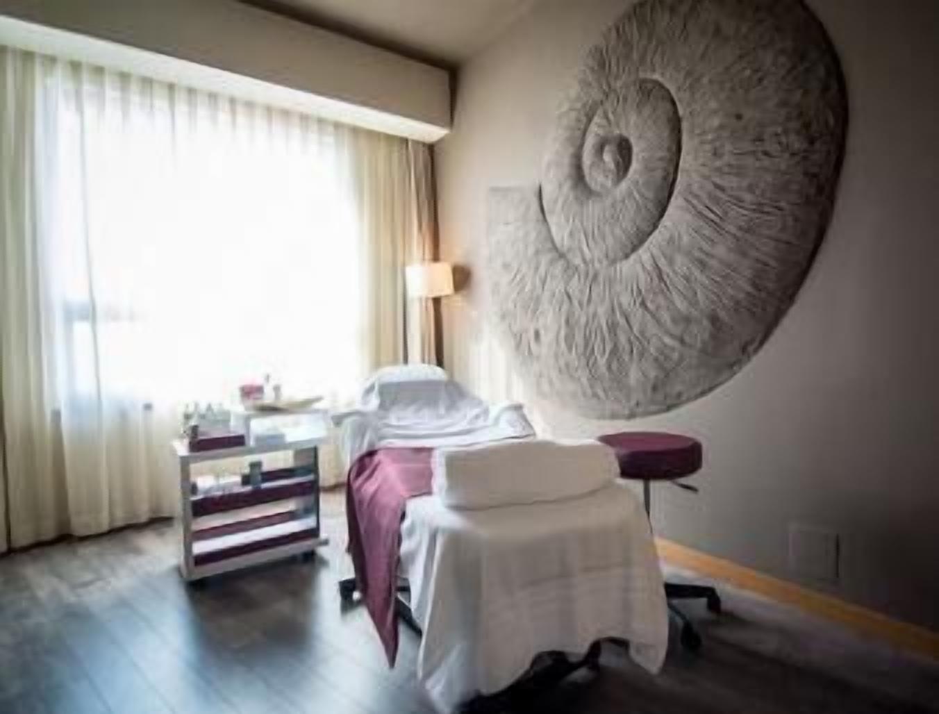 A hotel room with a bed, a bedside table, a lamp, a large abstract wall art, and a window with curtains.