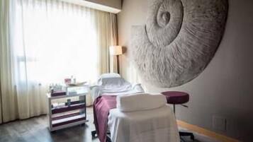 A hotel room with a bed, a bedside table, a lamp, a large abstract wall art, and a window with curtains.