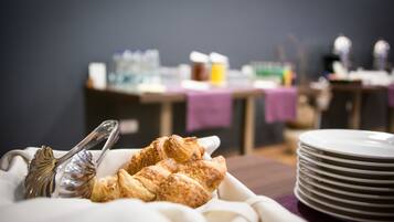 Une table mise pour le petit-déjeuner, avec des croissants et des couverts, et des assiettes empilées à proximité.
