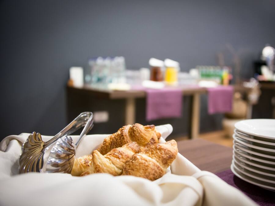 Une table mise pour le petit-déjeuner, avec des croissants et des couverts, et des assiettes empilées à proximité.