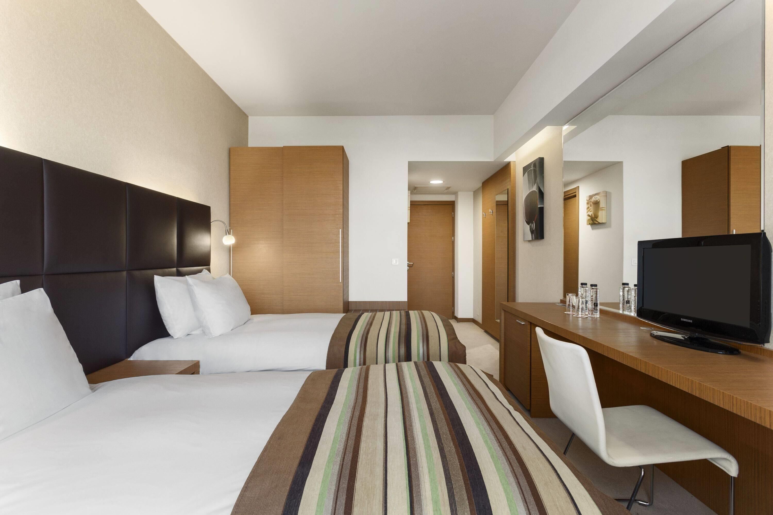 Habitación de hotel con dos camas, un escritorio con televisor y un espejo.