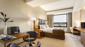 A hotel room with a bed, desk, chair, and a window with a view.